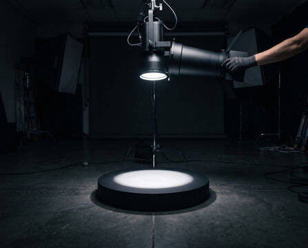 Technician adjusts a snoot spotlight to narrow a light beam onto an empty product podium in a dark studio