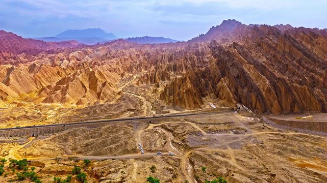 Aerial footage of a railway track passing through rugged desert mountain ridges and arid valleys in the Red Mountain Stone Forest, Kuqa, Xinjiang, China