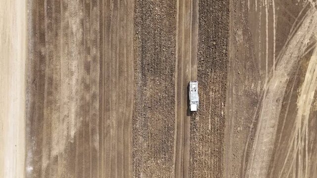 Earthmoving machines operate across broad agricultural fields in the Po Valley, Italy, with parallel tire tracks and graded soil defining the work area, top down parallax tilt