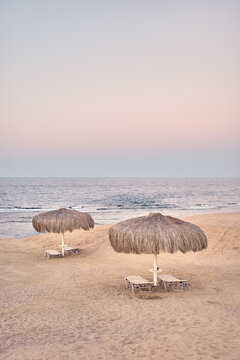 Straw beach umbrella and lounge chairs on a sandy beach, color toning applied.