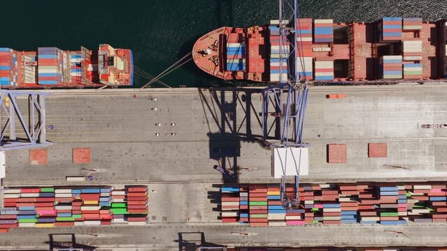 Overhead aerial shot capturing a massive cargo ship docked at a bustling commercial port, with gantry cranes actively unloading colorful shipping containers from the vessel onto the pier