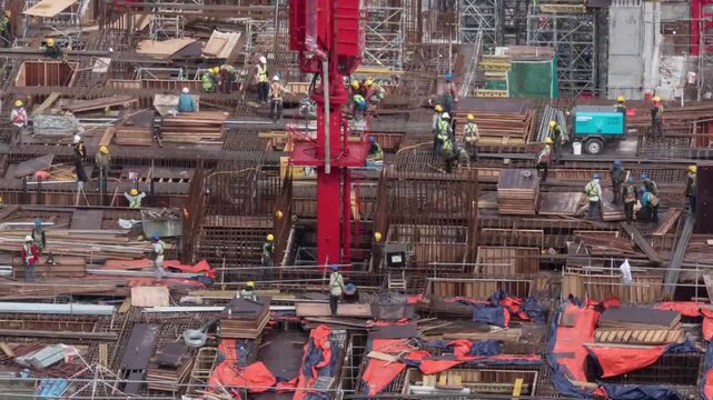 Aerial view of construction workers installing steel rebar foundation with heavy red tower crane