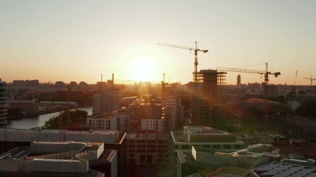 Morning sunrise over urban skyline with active construction site and multiple tower cranes