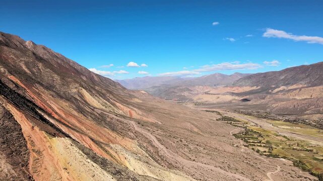 Color-banded slopes of Cerro General San Mart&iacute;n drop to the R&iacute;o Grande valley and farmland under clear blue sky, seen from a high drone flyover.