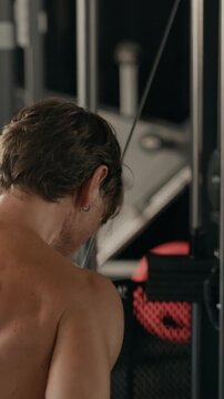 Vertical of Caucasian young adult man performing cable triceps pushdowns in gym, rear view. Footage suits sports marketing, fitness apps, bodybuilding campaigns, and athletic training commercials