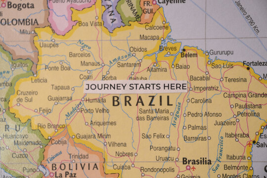 Overhead view of a typewriter-stamped cardstock ticket reading journey starts here resting on a physical map of Brazil