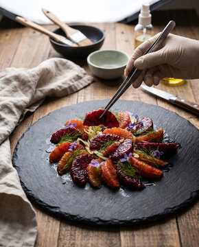 Food stylist placing final citrus segment on black slate platter salad
