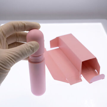 Packaging designer pressing applicator cap onto cosmetic tube beside open folding carton