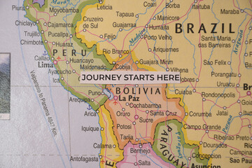 Obraz premium Overhead shot of a handwritten paper tag reading journey starts here resting on a physical map of Bolivia