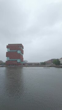 September 10, 2026 - Iconic MAS Museum in Antwerp, Belgium on a cloudy day with a boat on the water. Vertical footage.
