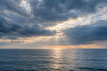 Fototapeta premium Sunlight Breaking Through Storm Clouds Over Calm Ocean