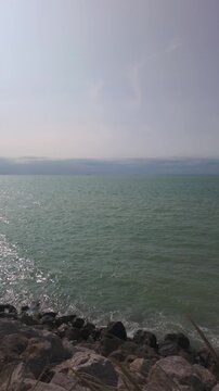 Vertical video of the tranquil sea lapping against a rocky coast on a hazy day