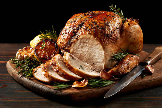 Sliced roasted turkey breast on wooden carving board with rosemary, garlic and charred lemon