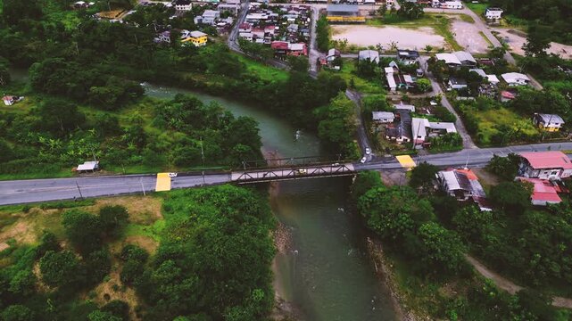 Drone View of River Bridge and Road Through Ecuador Town, Green Water, Forested Banks, Urban Buildings and Tropical Infrastructure Scene