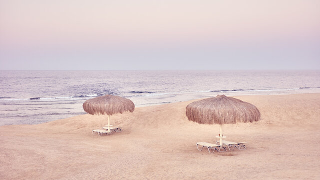 Straw beach umbrellas and lounge chairs on a sandy beach, color toning applied.