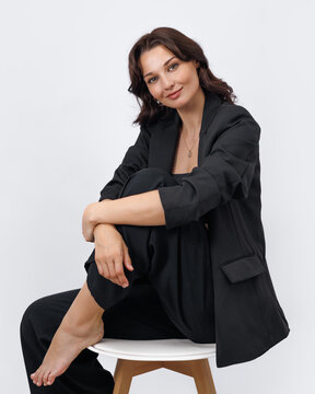Confident Young Woman in Black Business Suit Sitting on White Stool