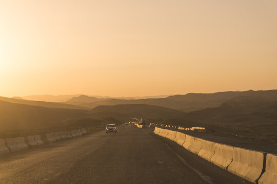 A road at sunset set against a backdrop of mountains and hills; clear skies and the warm rays of the setting sun; a travel-themed atmosphere suitable for a background