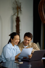 Happy couple going through paperwork while using laptop at home.