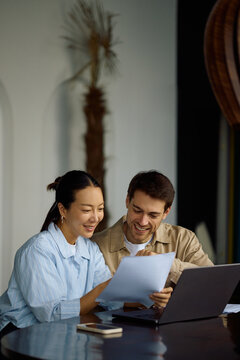 Happy couple going through paperwork while using laptop at home.