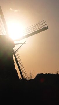 Vertical video of a silhouetted Dutch windmill with turning blades against a beautiful sunset sky.