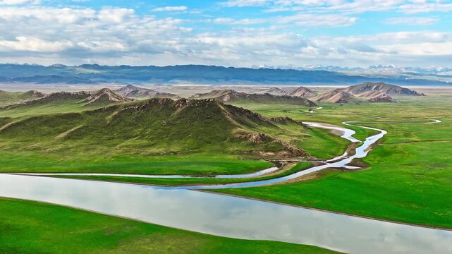 Aerial view of a meandering river flowing through lush green meadows in Bayinbuluke Grassland, Xinjiang, China