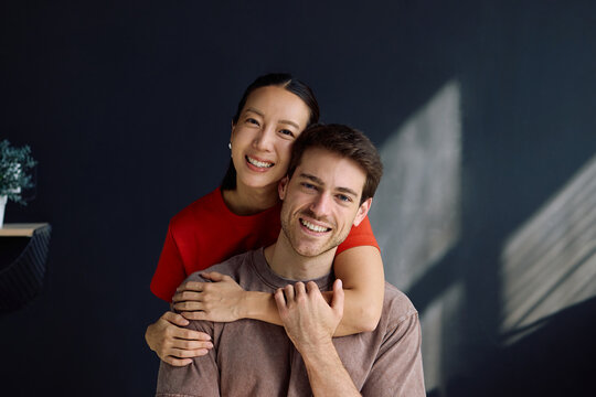 Happy embraced couple at home looking at camera.