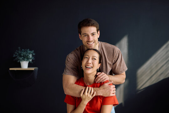Happy man embracing his Korean wife and looking at camera.