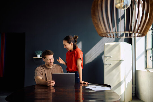 Happy couple talking while using laptop at home.