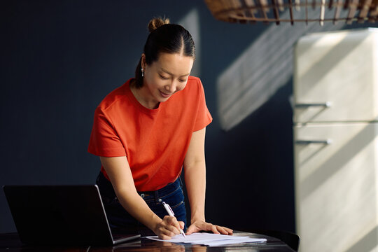 Happy Korean entrepreneur going through paperwork while working at home.