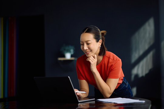 Happy Korean woman using laptop while working at home.