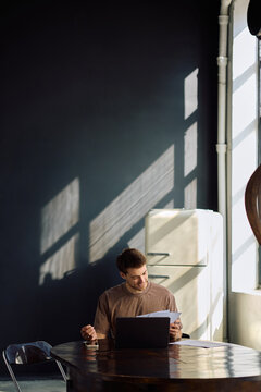 Happy male entrepreneur going through paperwork while working on laptop at home.