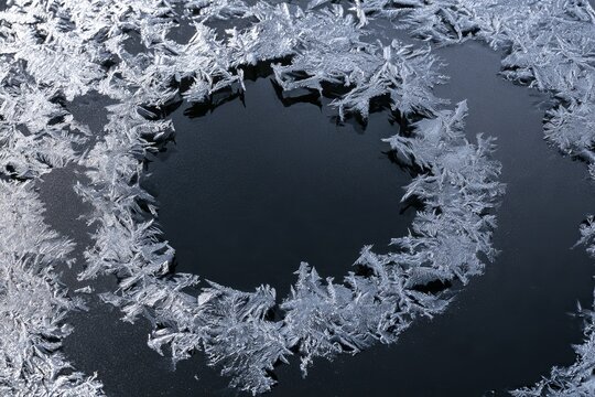 Frost patterns form a circular design on a surface during a cold winter morning