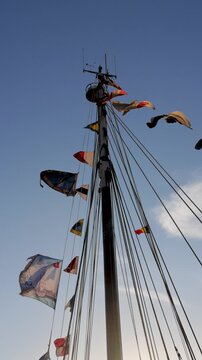 September 10, 2026 - Vertical video of a tall ship's mast with various international flags waving in the wind against a clear blue sky.