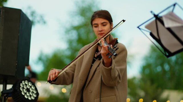Young musician playing violin outdoors during a serene evening performance with warm string music, soft lights, and a peaceful natural green background