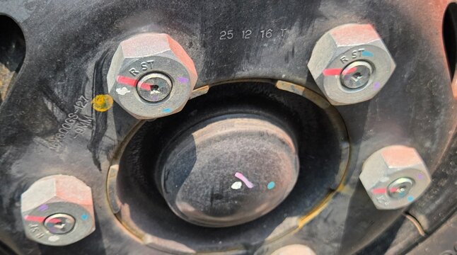 Close-up of heavy-duty truck wheel lug nuts with right-hand thread markings and torque seals