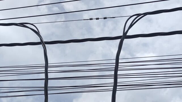 Pan right video of disconnected twisted aerial cables hanging under a cloudy sky ready for jointing, industrial electrical power grid and overhead distribution network maintenance.