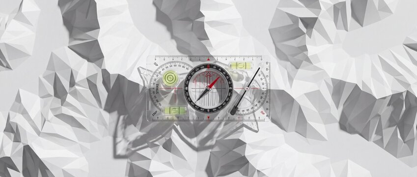 Transparent geological compass sits atop white low poly paper relief model representing mountain range for topographical elevation study