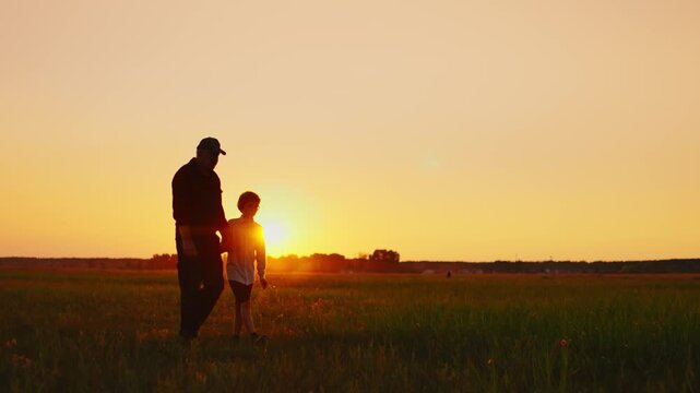 Silhouetted father and son walking hand in hand through a peaceful meadow at sunset, sharing a quiet moment together in the warm golden evening light