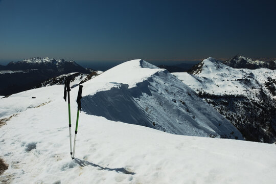 Hiking poles on the wonderful snow-covered ridge of Monte Araralta. In the background, the peaks Resegone (left), Sodadura and Grigna meridionale (right). Orobie Prealps, Lombardy, Italy.