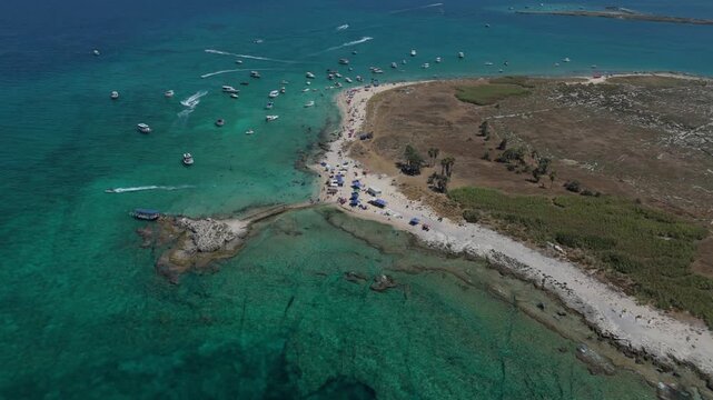 An aerial drone view showing a crowded beach with turquoise water, anchored boats, and jet skis off Rabbit Island in Tripoli, Lebanon.