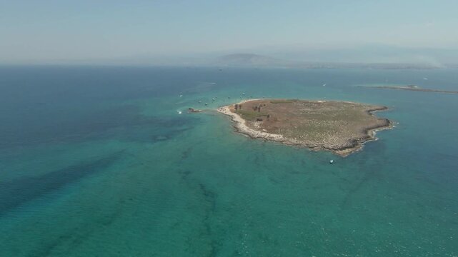 An aerial shot shows a small, rocky island surrounded by clear turquoise and deep blue sea in Tripoli, Lebanon.