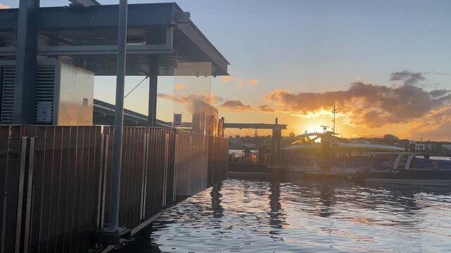 Passengers disembark from a ferry at the terminal beneath a vivid orange sunset, capturing everyday waterfront travel in warm evening light.