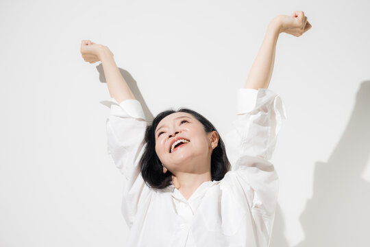 白背景で両手を高く伸ばしてストレッチする50代女性、健康的な生活とリフレッシュを楽しむ爽やかな笑顔のミドル世代　更年期やヘルスケアなどのイメージ	

