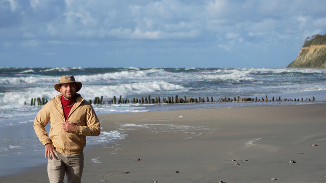 Confident man in a beige jacket standing on a scenic coastline during an autumn travel journey.