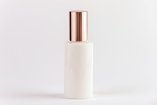 A sleek, white cosmetic bottle with a shiny rose gold cap, set against a plain, light background.