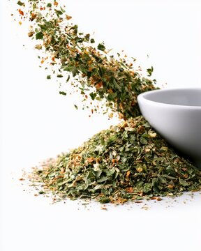 A close-up of dried mixed herbs spilling from a white bowl onto a white surface, highlighting various green, orange, and brown flakes.