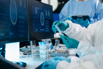 Medical researchers in PPE analyze a biological sample in a test tube and digital brain scans on...