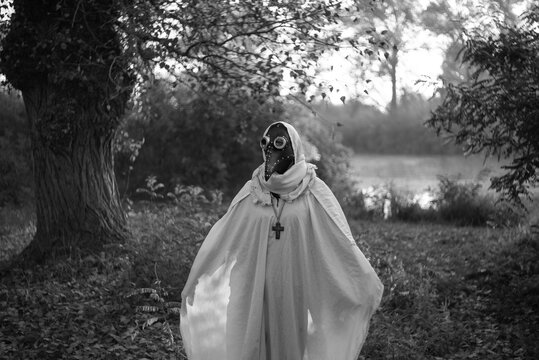 Mysterious masked woman standing alone in autumn Halloween landscape.