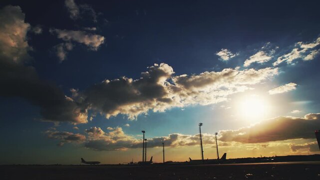 Golden hour at the airfield featuring dramatic clouds and silhouettes of commercial aircraft on the tarmac