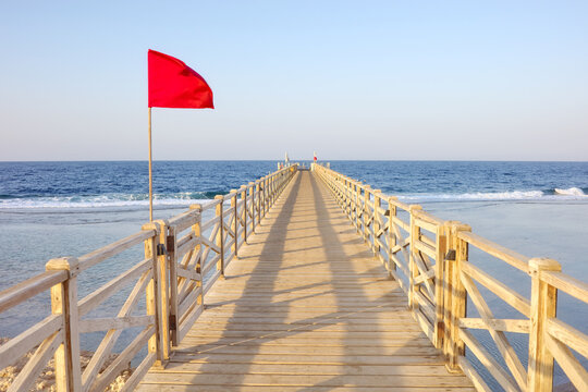 A wooden pier with a red warning flag at sunset.